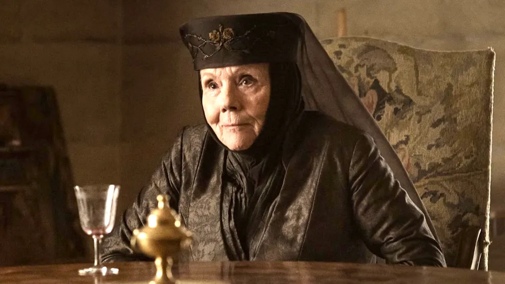 Diana Rigg as Olenna Tyrell sitting at a table in Game of Thrones.