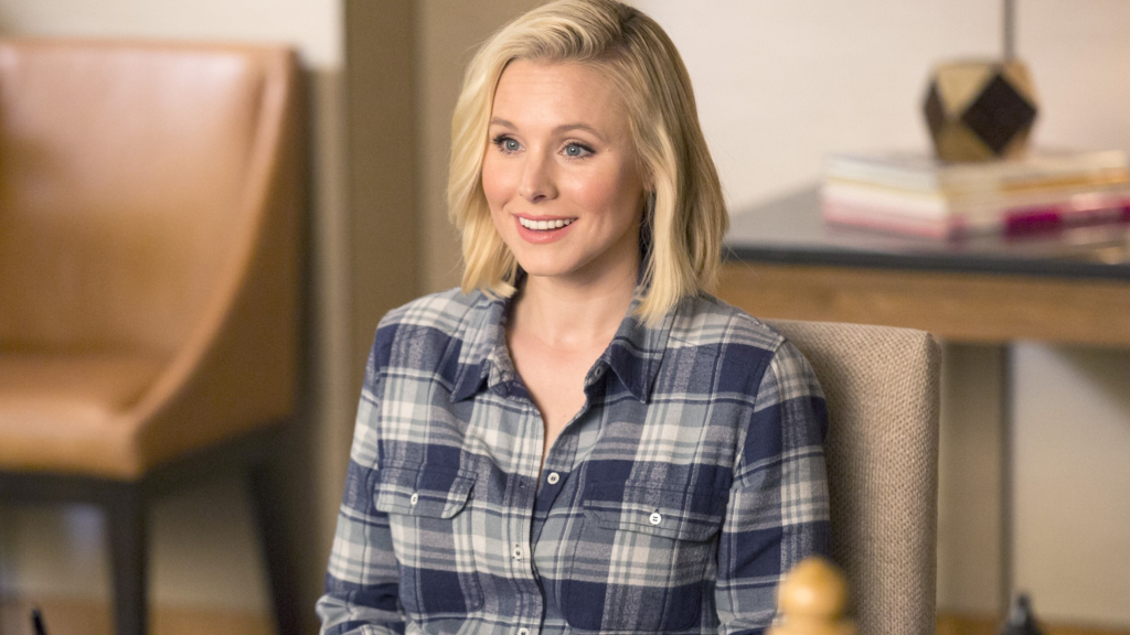 Eleanor wearing a flannel and smiling while sitting in The Good Place