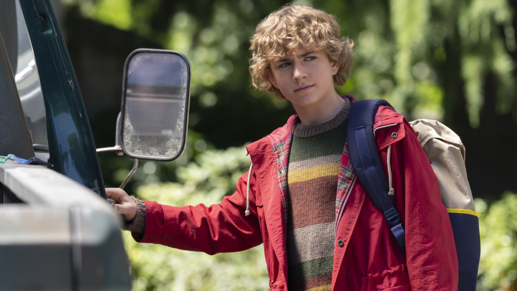 Walker Scobell as Percy Jackson wearing a red jacket and opening the door of a truck in Percy Jackson & the Olympians