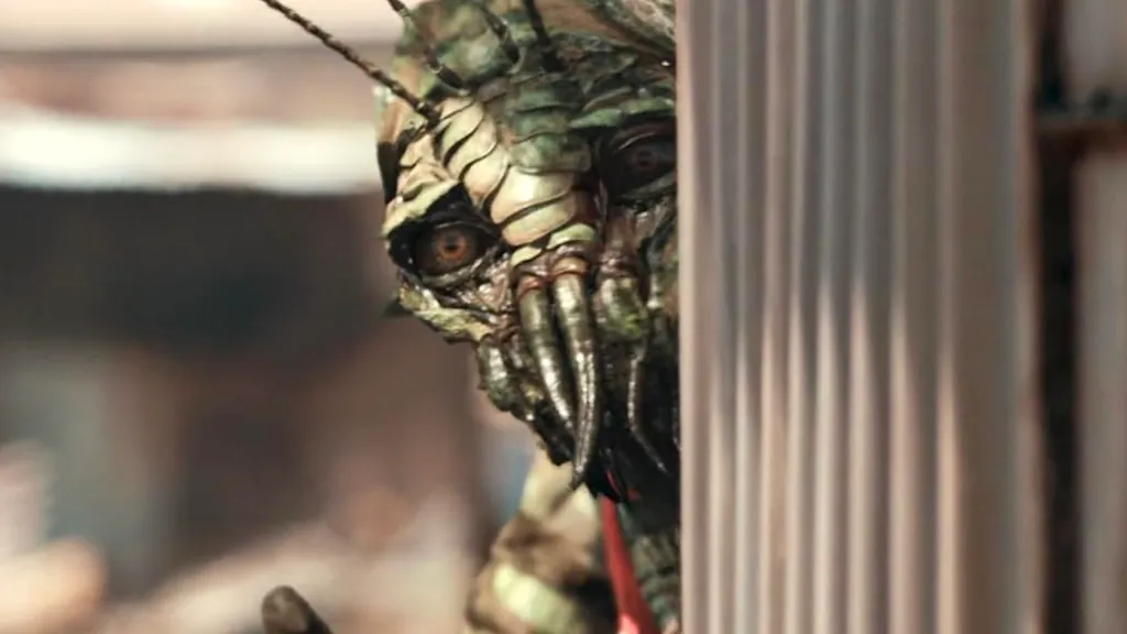 A green Alien peeking out from behind a wall in District 9.