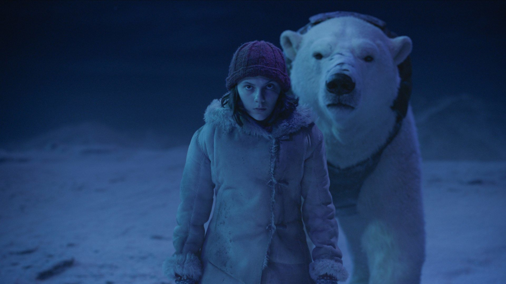 Dafne Keen as Lyra standing next to Iorek in His Dark Materials