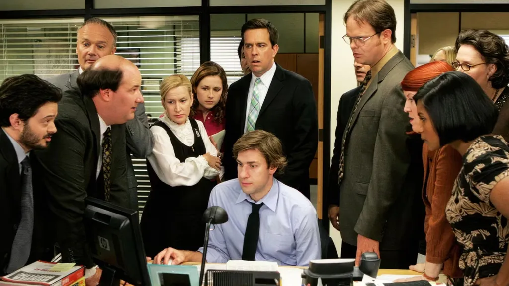 The cast of The Office surrounding Jim's desk together.